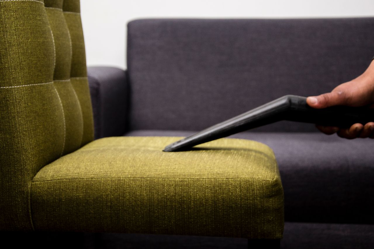 services-01 Close-up of a person vacuuming a modern sofa chair indoors, highlighting cleaning service.